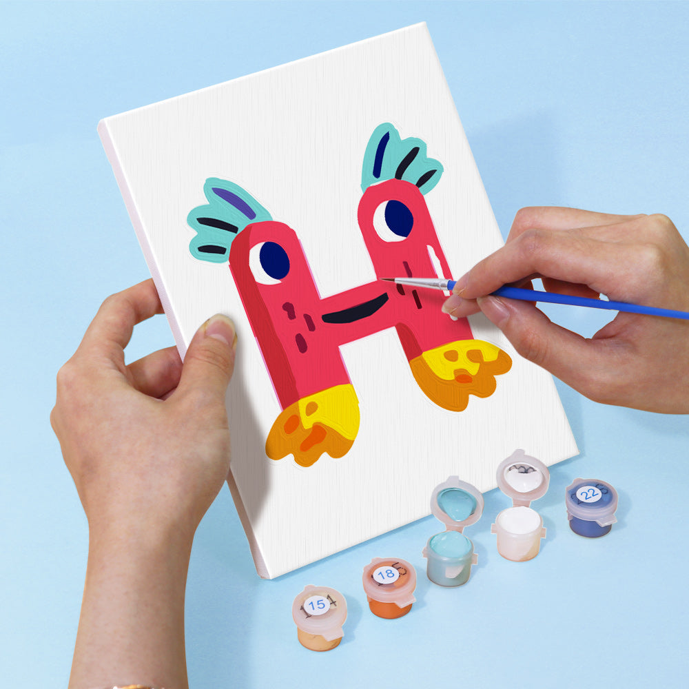 Person painting a colorful letter 'H' on a white canvas with paint containers below.