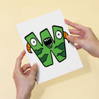 Hands holding a card with a green monster letter 'W' design on a beige background
