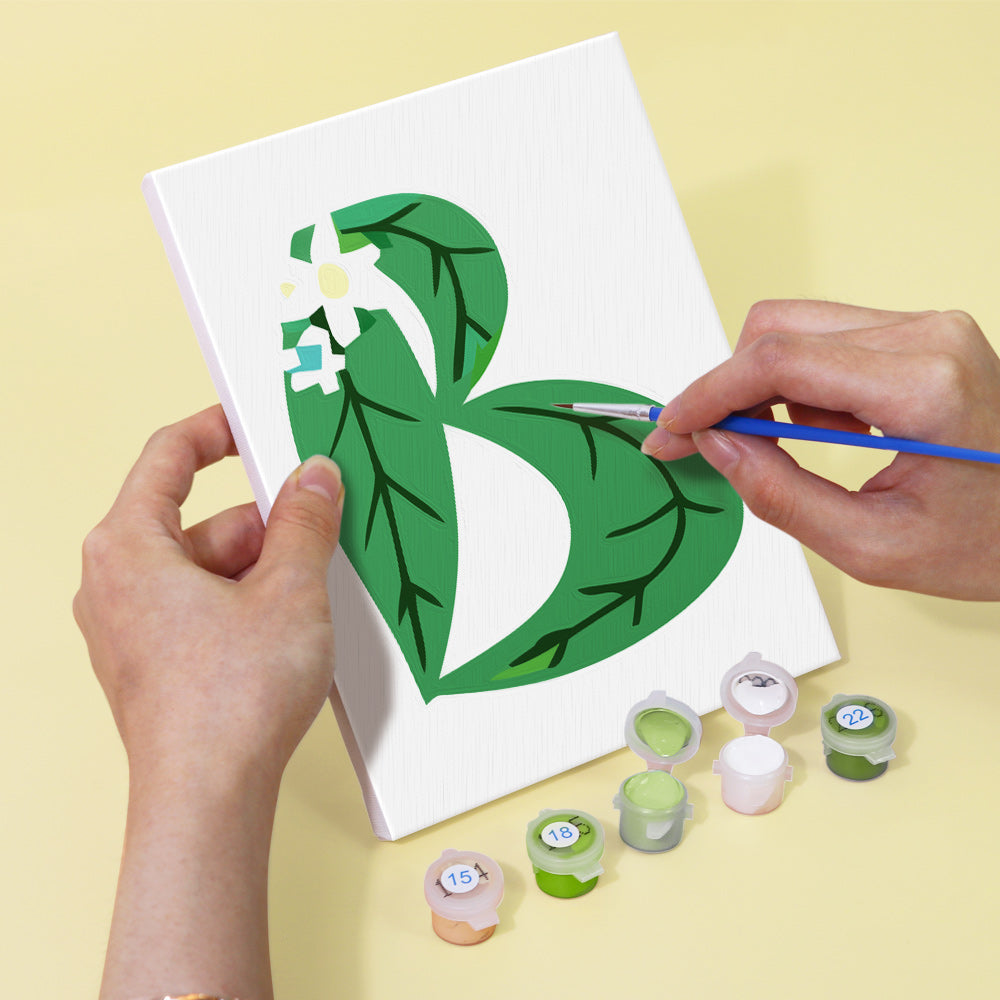 Person painting a green leaf design on a white canvas with paint supplies.