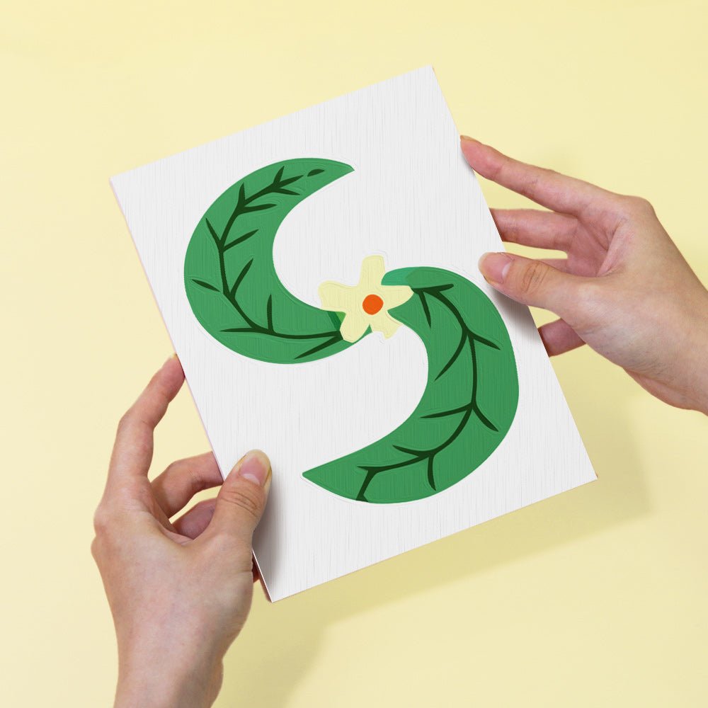 Card with green leaf design held by hands against a yellow background