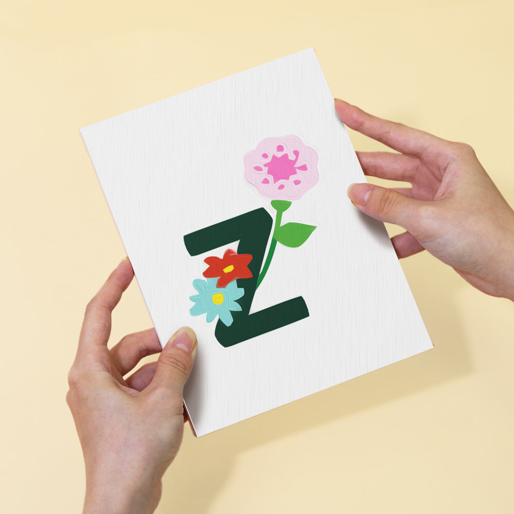 Card with letter 'Z' and flowers held by hands against a yellow background
