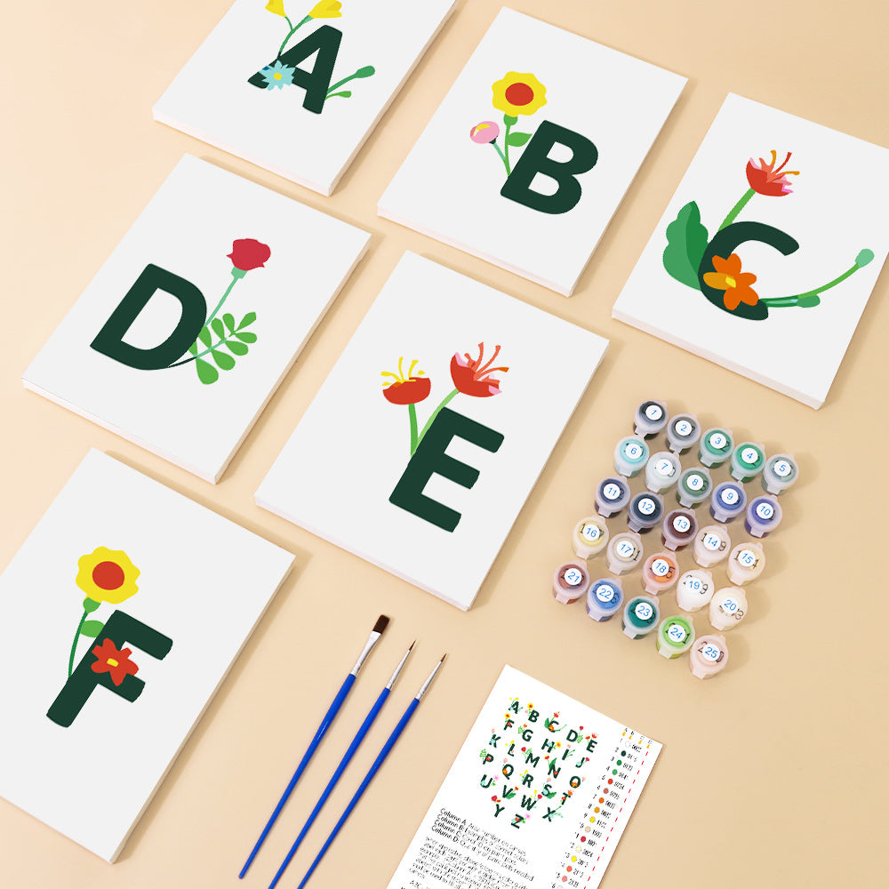 Alphabet cards with floral designs and painting supplies on a beige surface