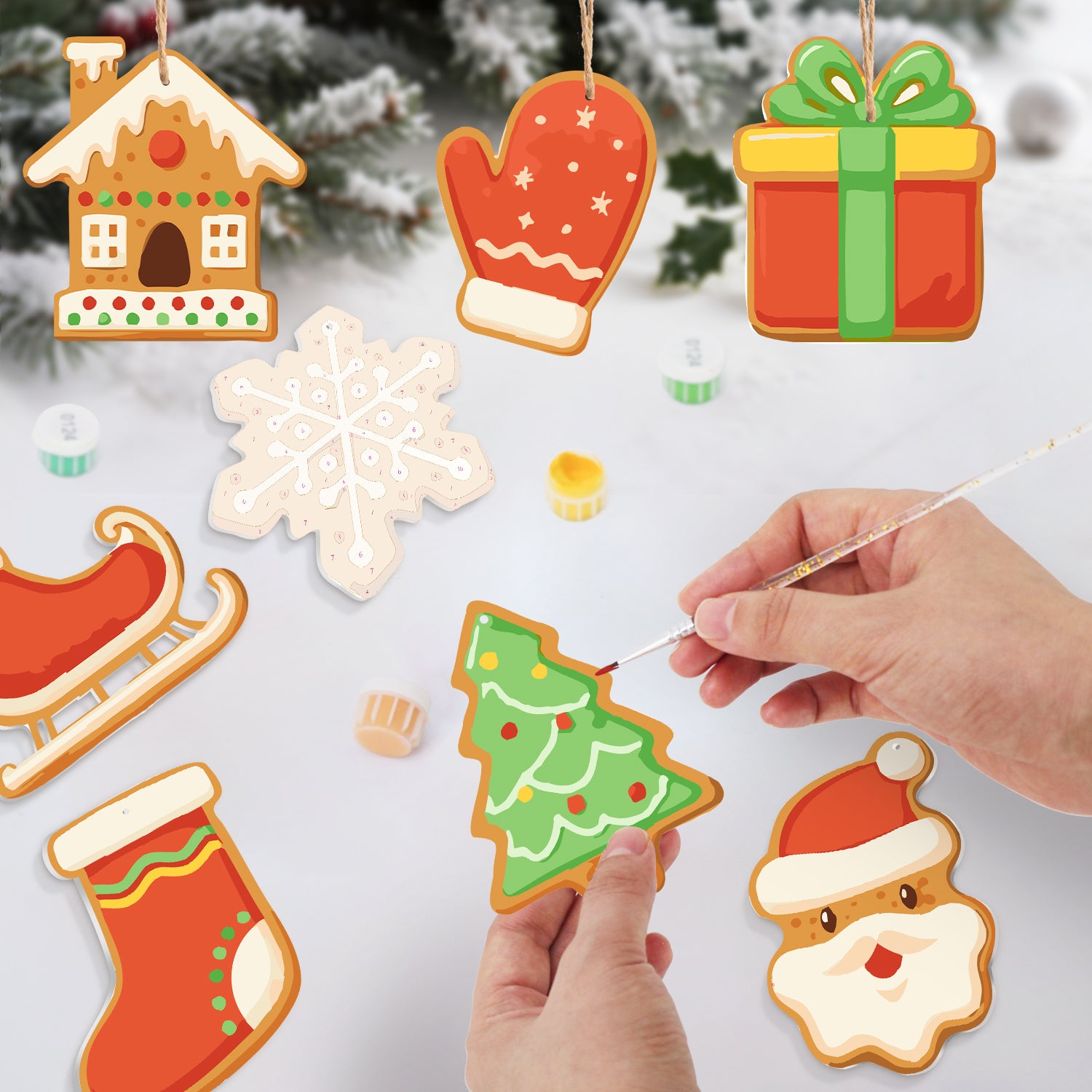 Decorative Christmas cookies shaped like a house, mittens, a gift, a snowflake, a tree, a sleigh, a stocking, and Santa Claus, with a hand painting a cookie.