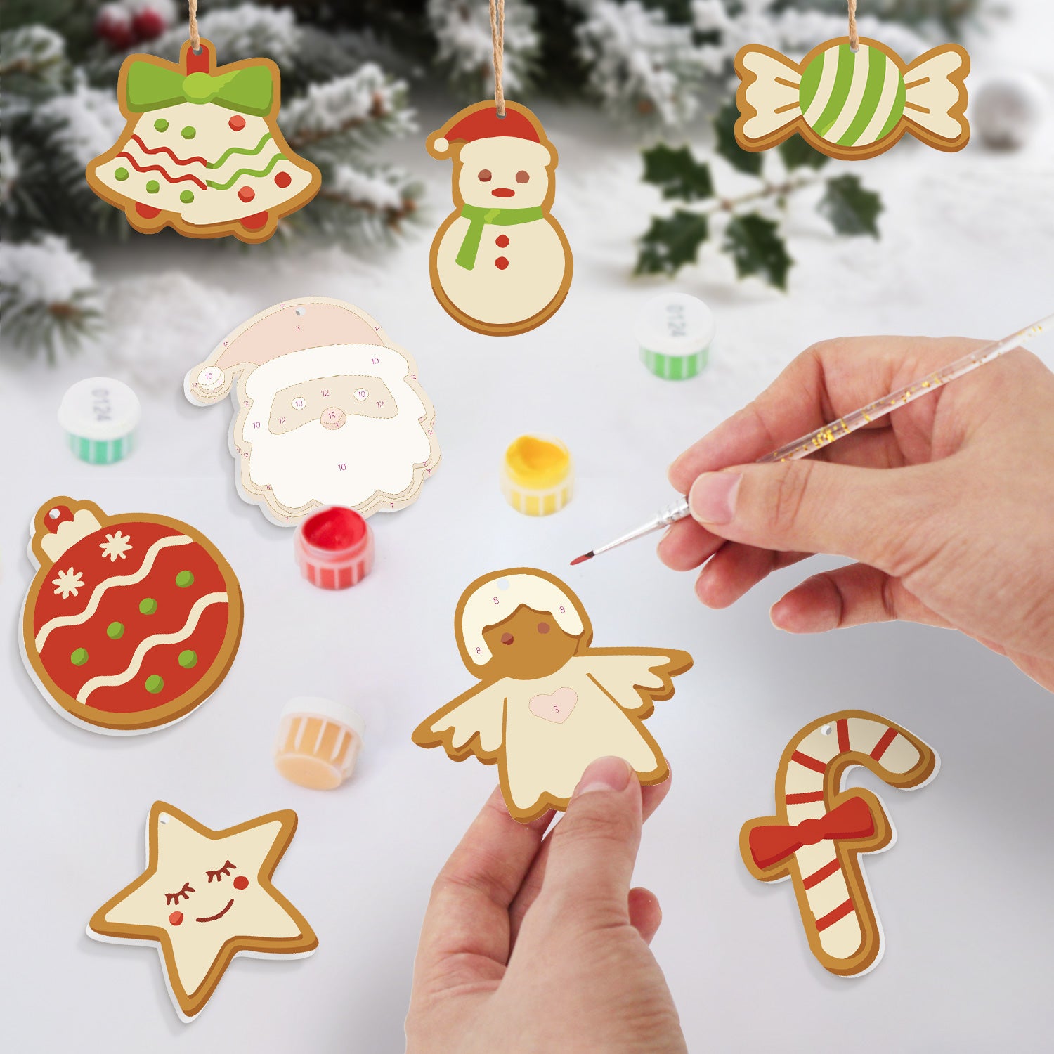 Galletas navideñas decorativas pintadas con una mano sosteniendo un pincel sobre un fondo nevado.