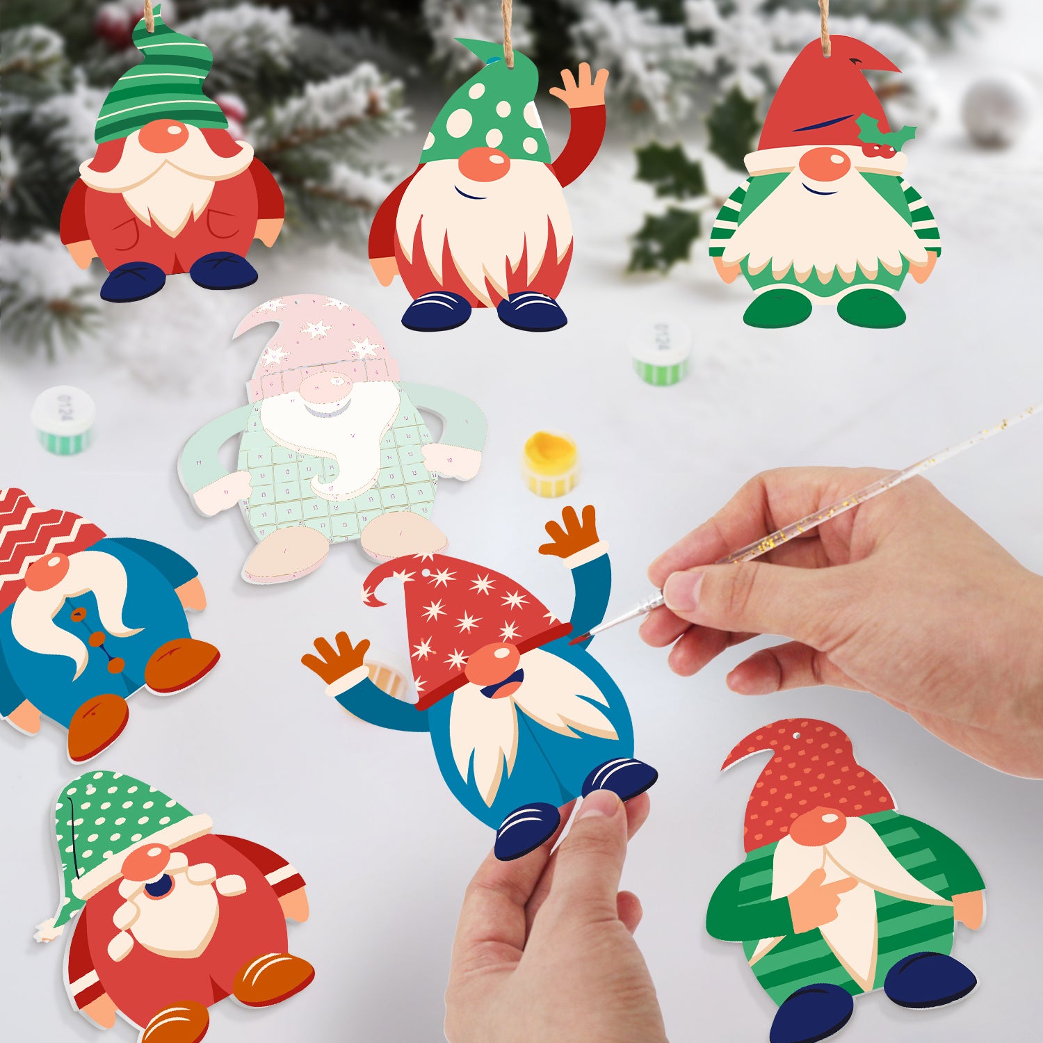 Colorful gnome ornaments with a hand holding a paintbrush against a snowy background