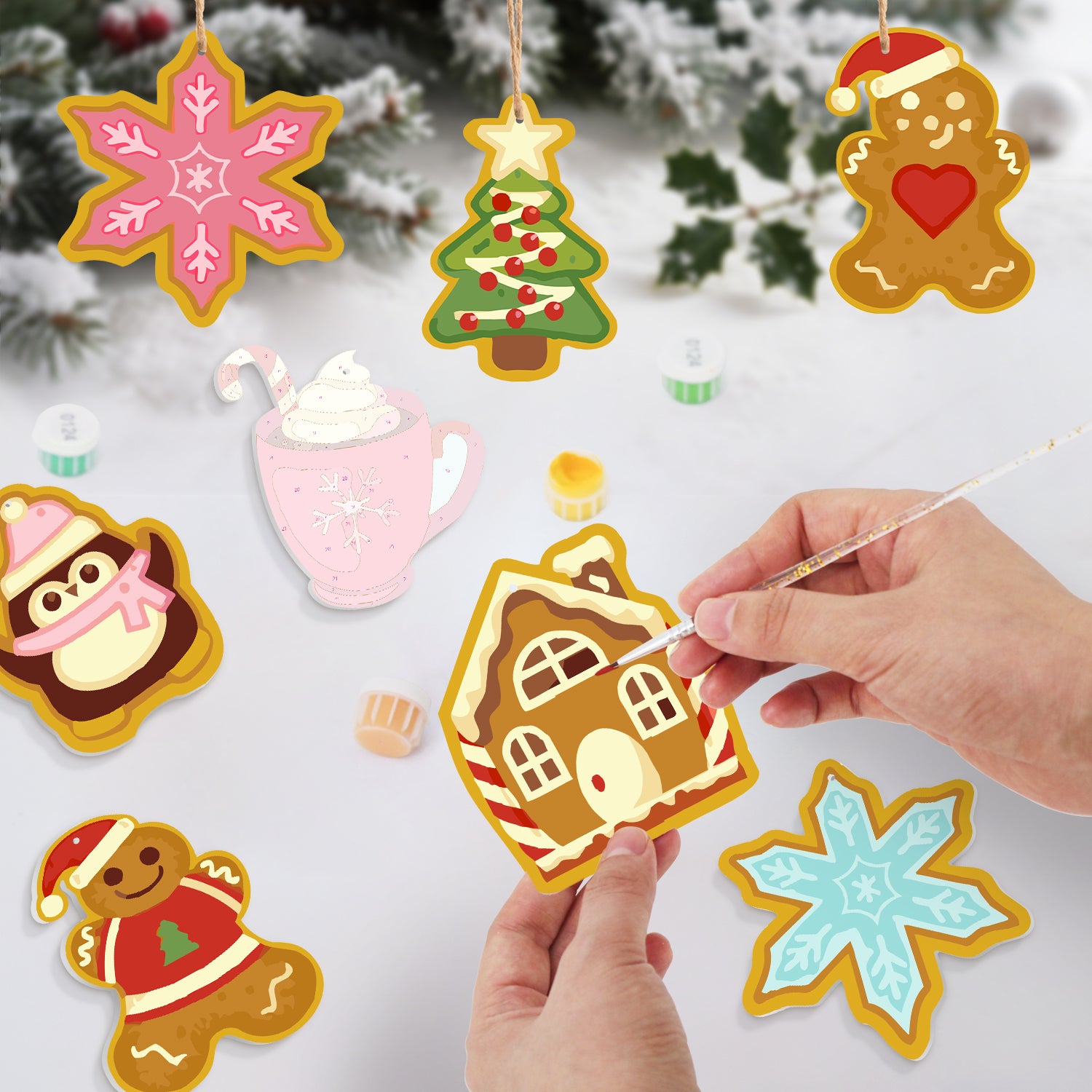 Decorative Christmas ornaments shaped like gingerbread houses, snowflakes, and trees on a snowy background.