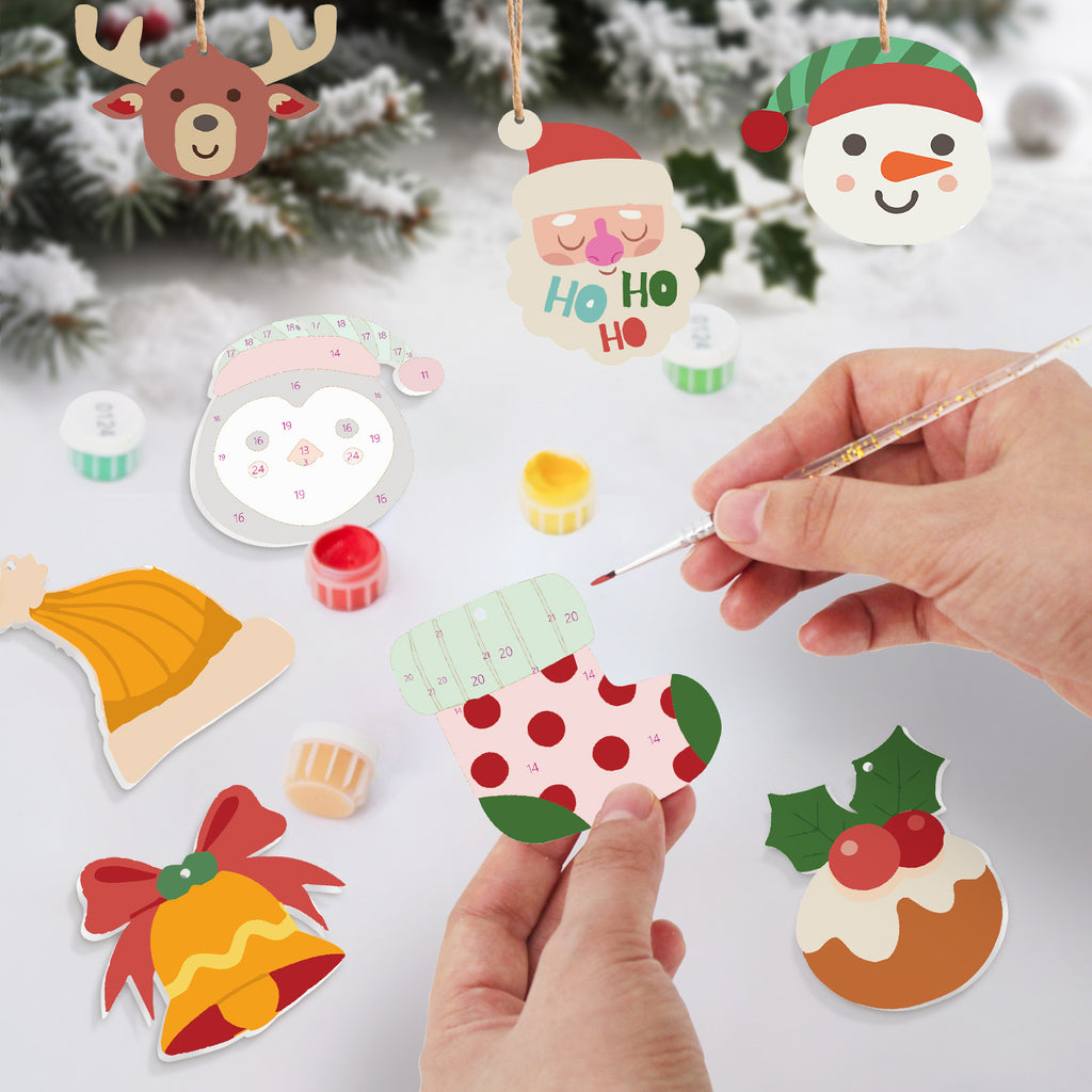 Handmade Christmas ornaments being painted with a brush on a white surface.