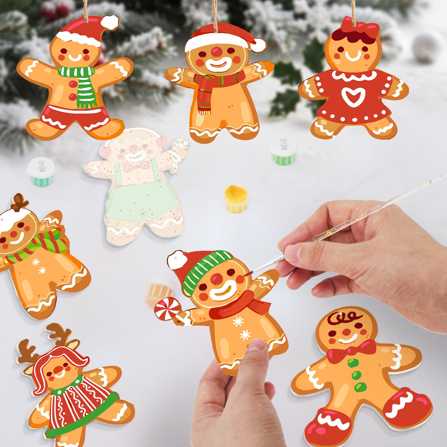 Decorative gingerbread ornaments being painted on a white surface with a Christmas tree in the background.