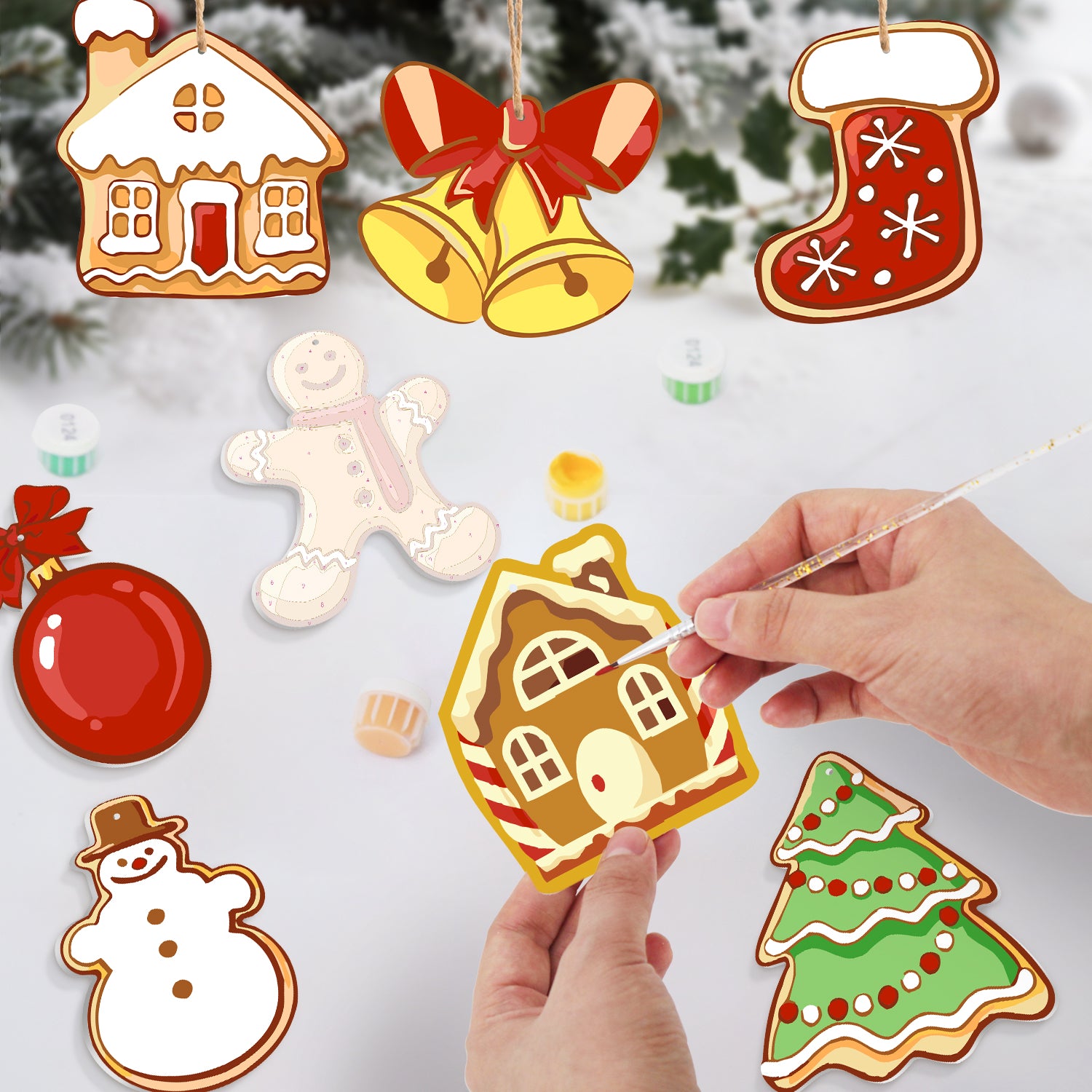 Ornements décoratifs de Noël comprenant une maison en pain d'épice, une cloche, un bas, un bonhomme en pain d'épice, un bonhomme de neige et un arbre sur fond enneigé.