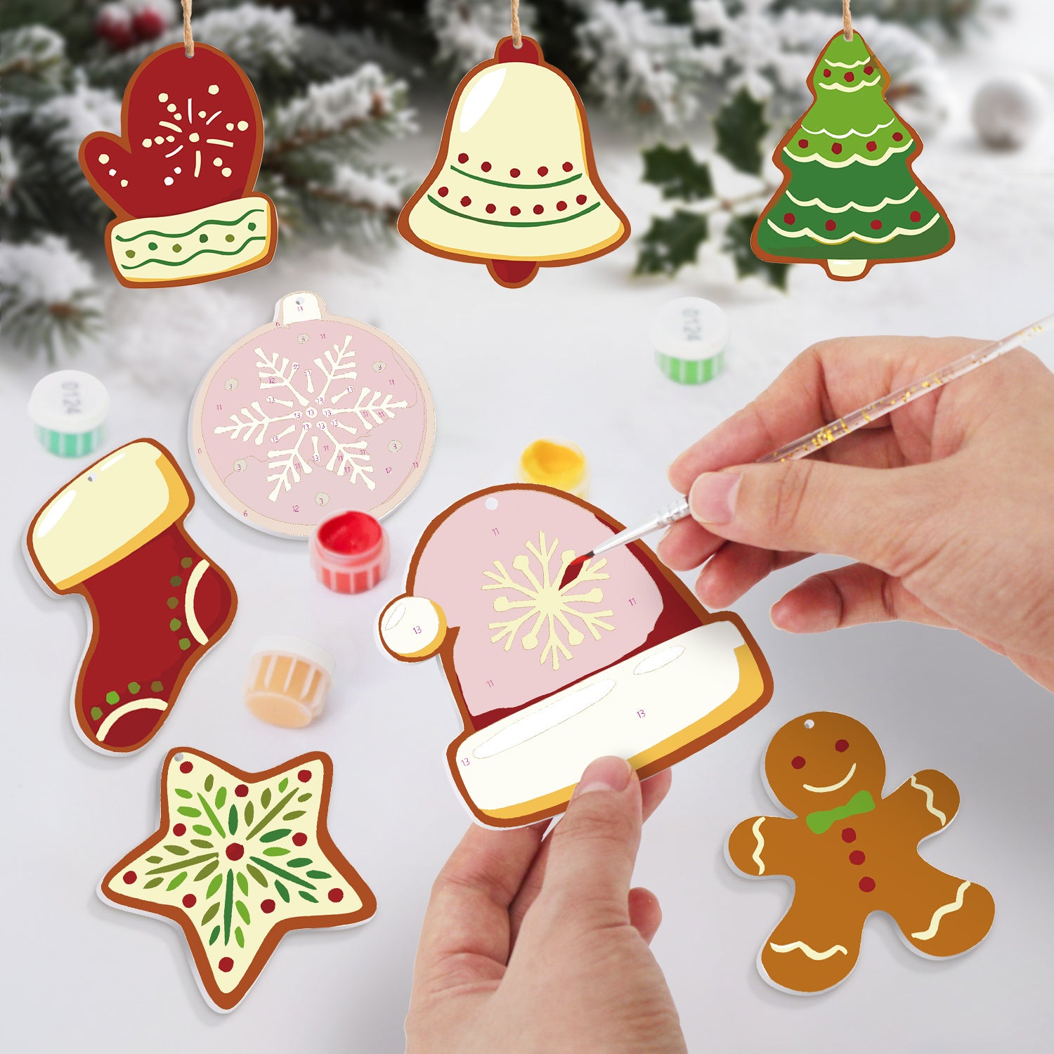 Decorative Christmas ornaments being painted with a hand holding a paintbrush against a snowy background.
