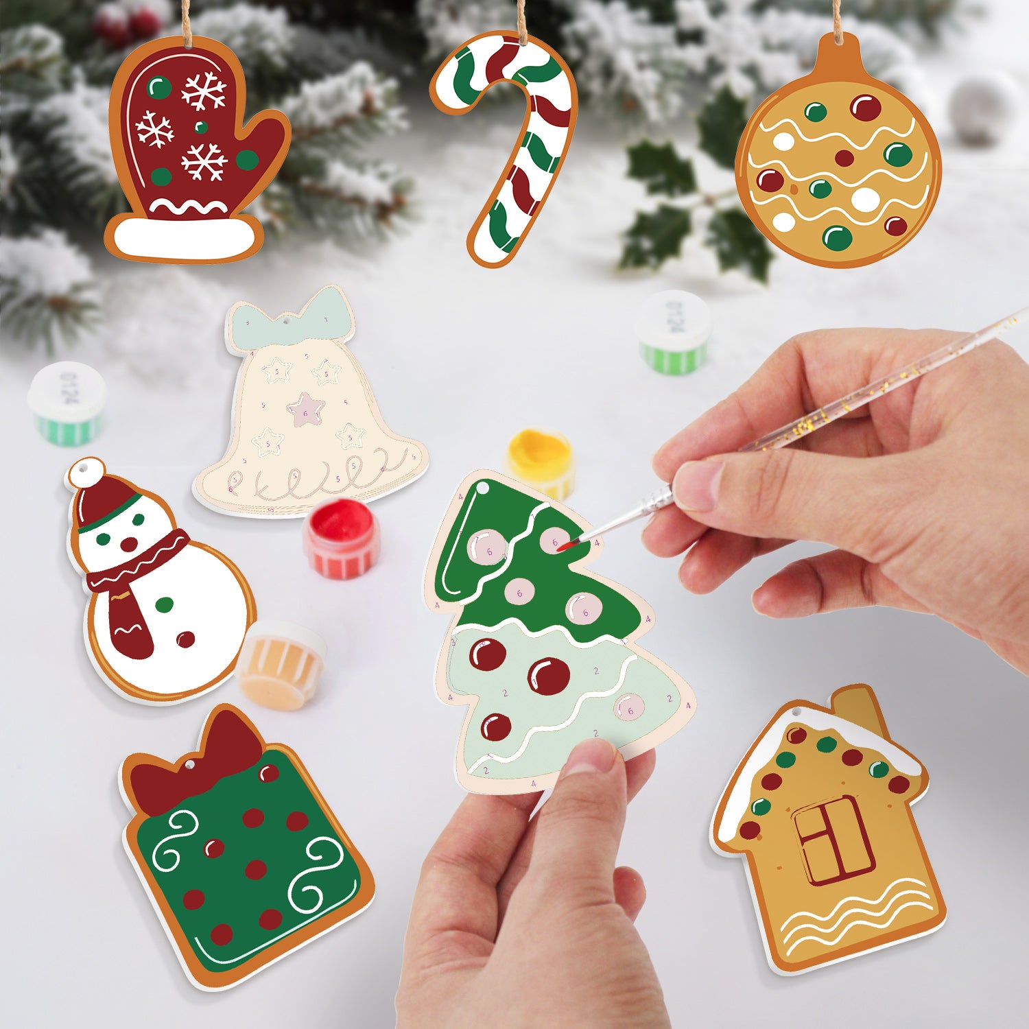 Decorative Christmas ornaments being painted with a hand holding a paintbrush against a snowy background.