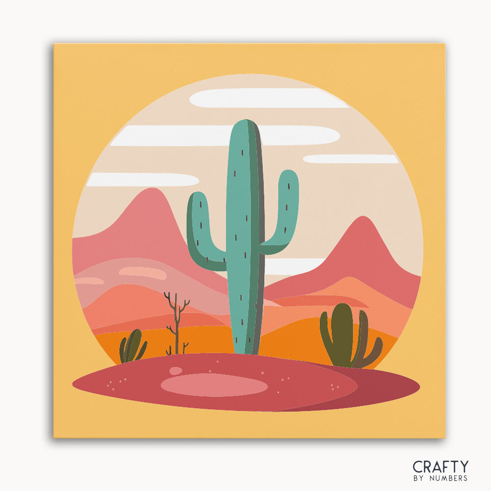 A paint by numbers kit depicting a desert scene with a tall cactus in the foreground and mountains in the background, predominantly in orange, pink, and green colors.