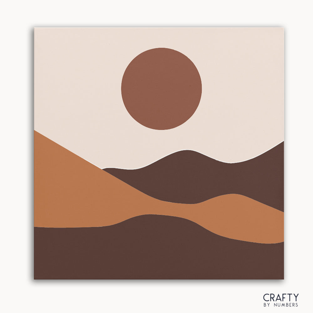 A minimalist paint by numbers kit depicting a desert landscape with sand dunes and a setting sun in earth tones.