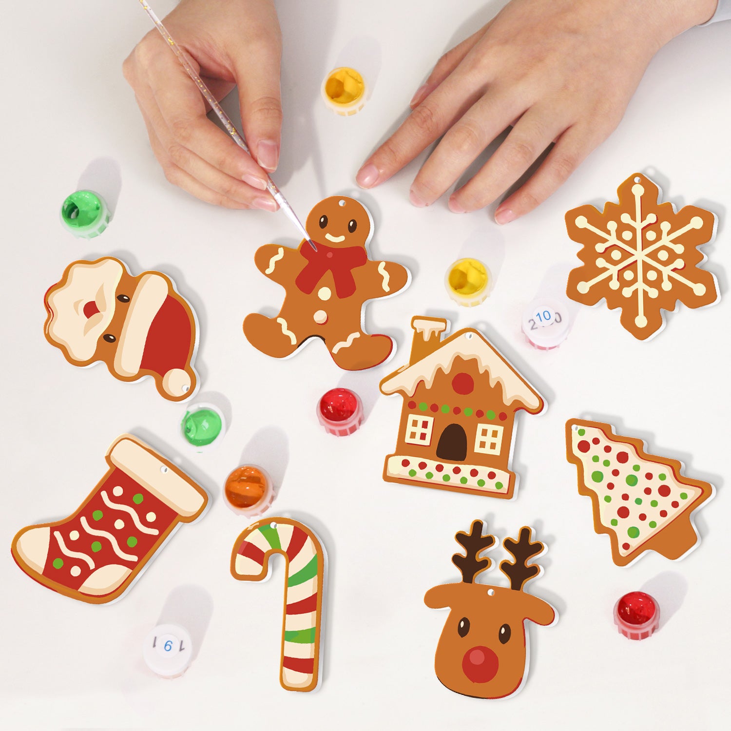 Decorative Christmas cookies being painted by hands on a white surface.