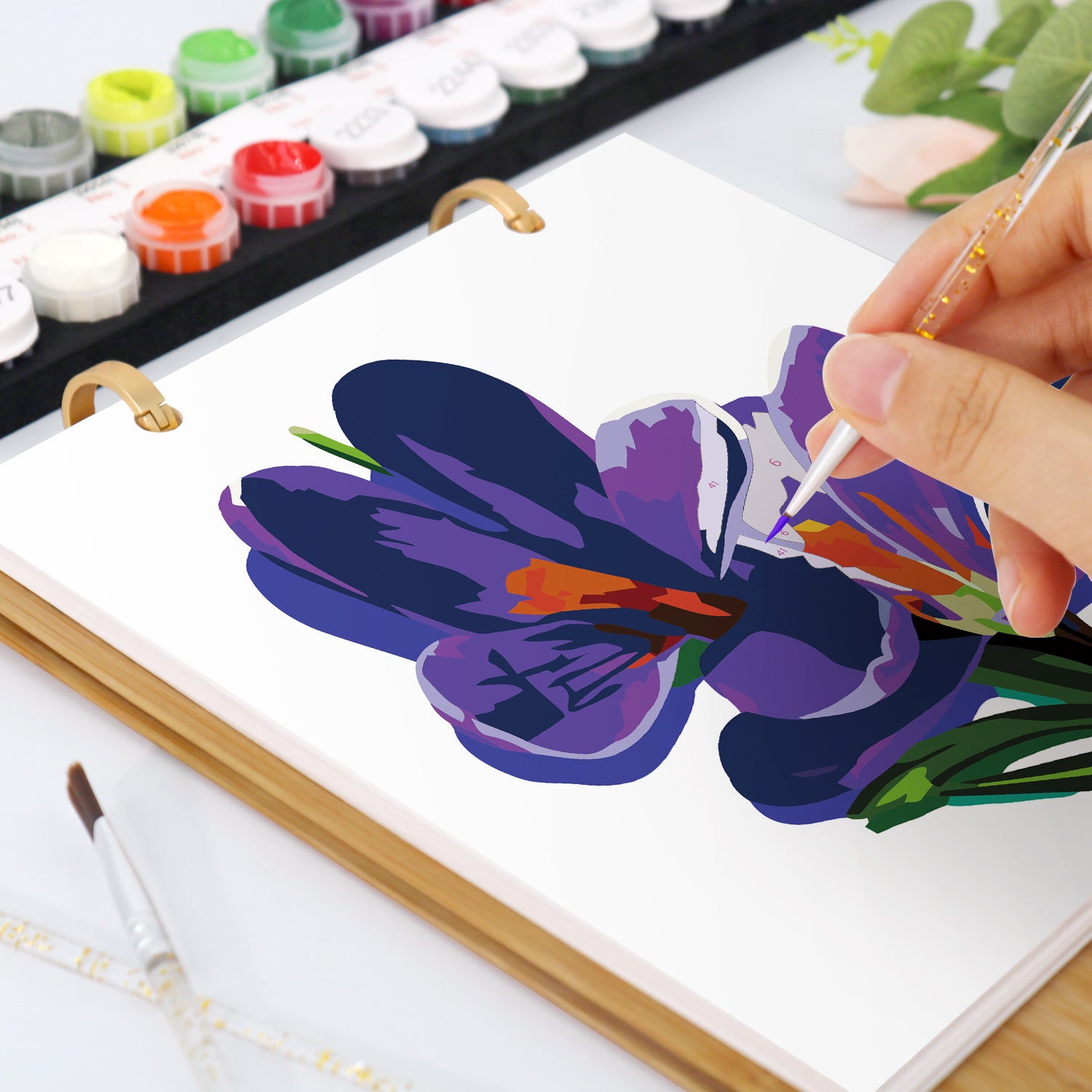 Person painting a purple flower on a canvas with watercolor paints.