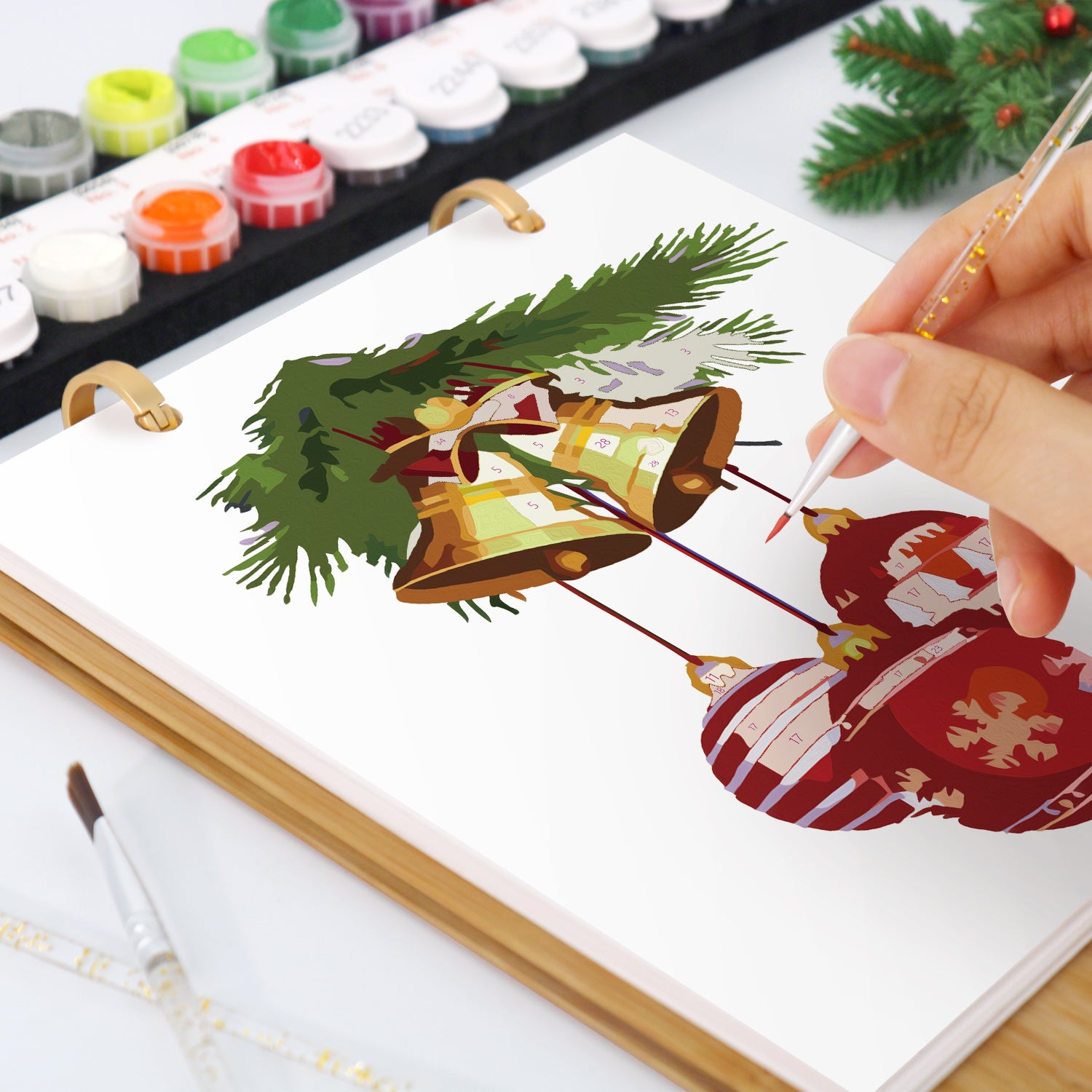 Representación artística de elementos de temática navideña, incluidas campanas y un árbol, sobre un lienzo con materiales de pintura.