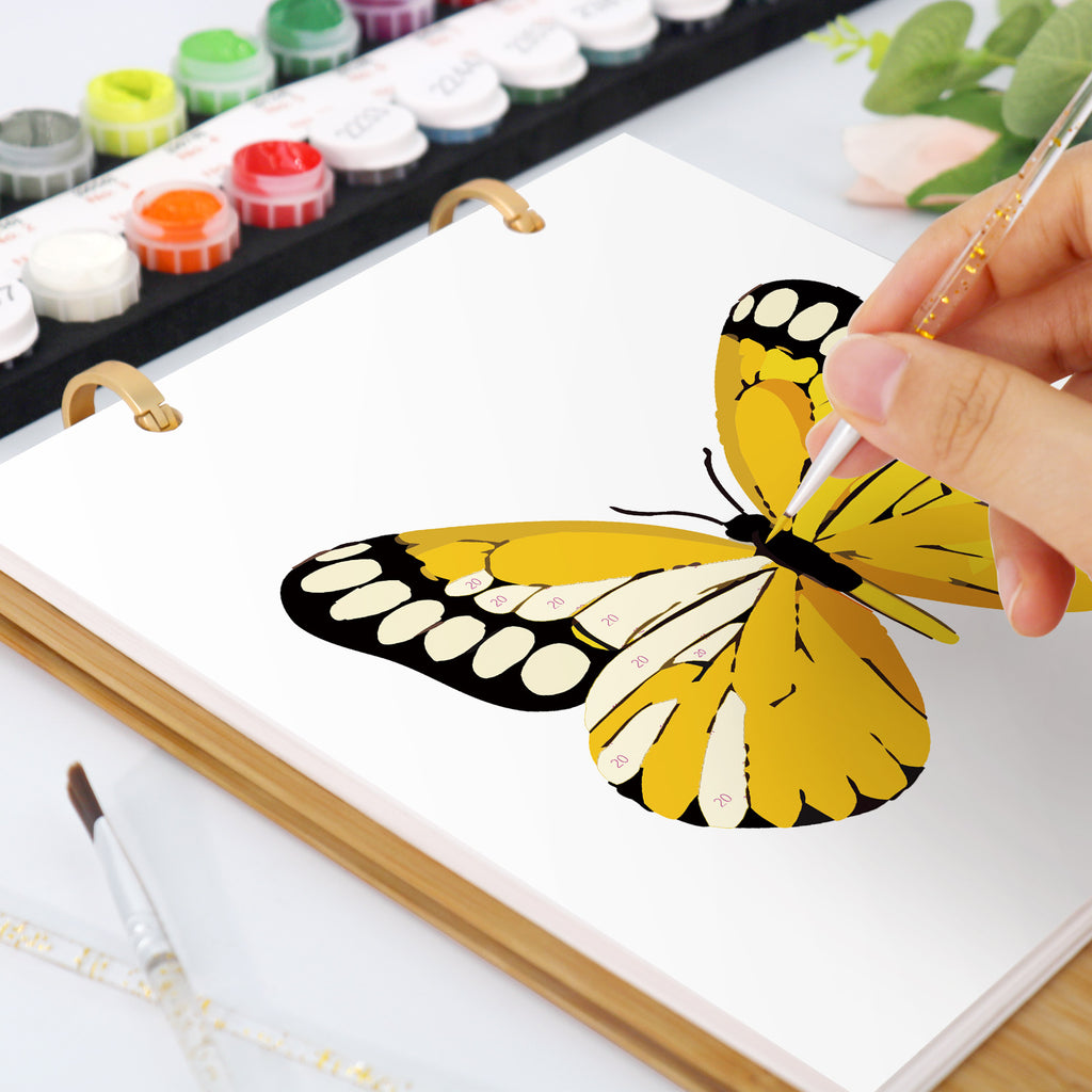 Person malt mit Aquarellfarben einen gelben Schmetterling auf eine weiße Leinwand.