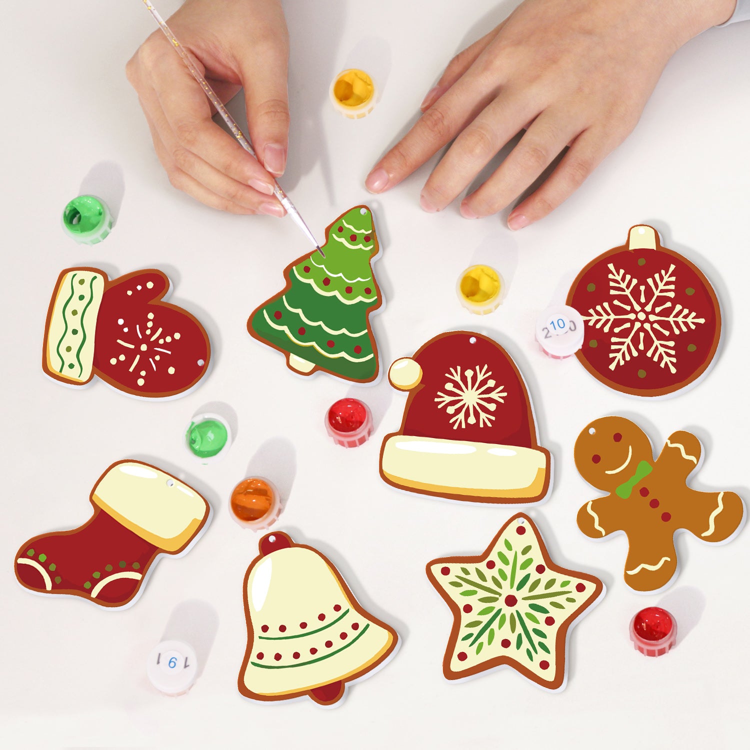 Decorative Christmas ornaments being painted by hands on a white surface.