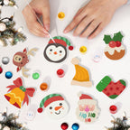 Children's hands decorating Christmas-themed stickers on a white surface with festive decorations around.