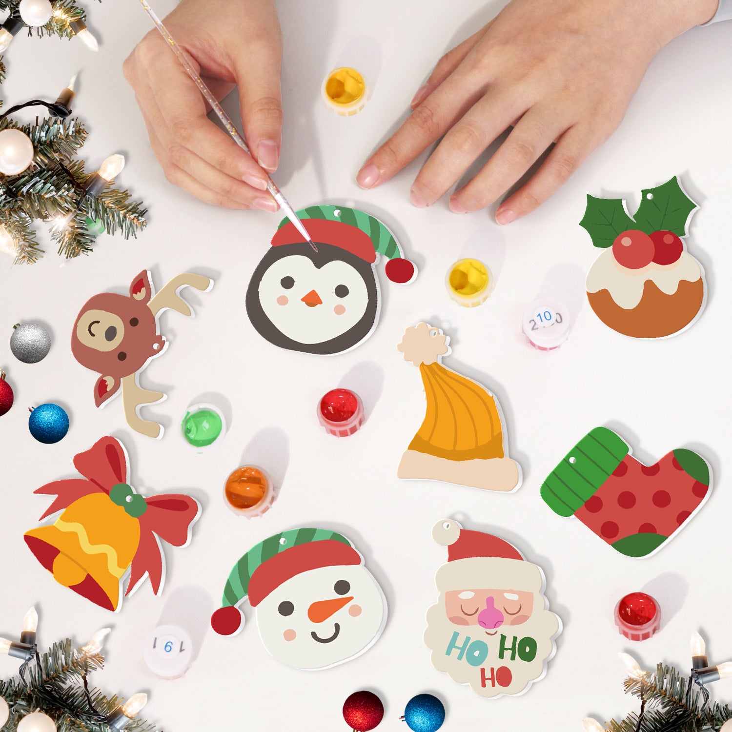 Children's hands decorating Christmas-themed stickers on a white surface with festive decorations around.