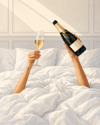 Two hands holding a champagne bottle and flute above rumpled white bedding.
