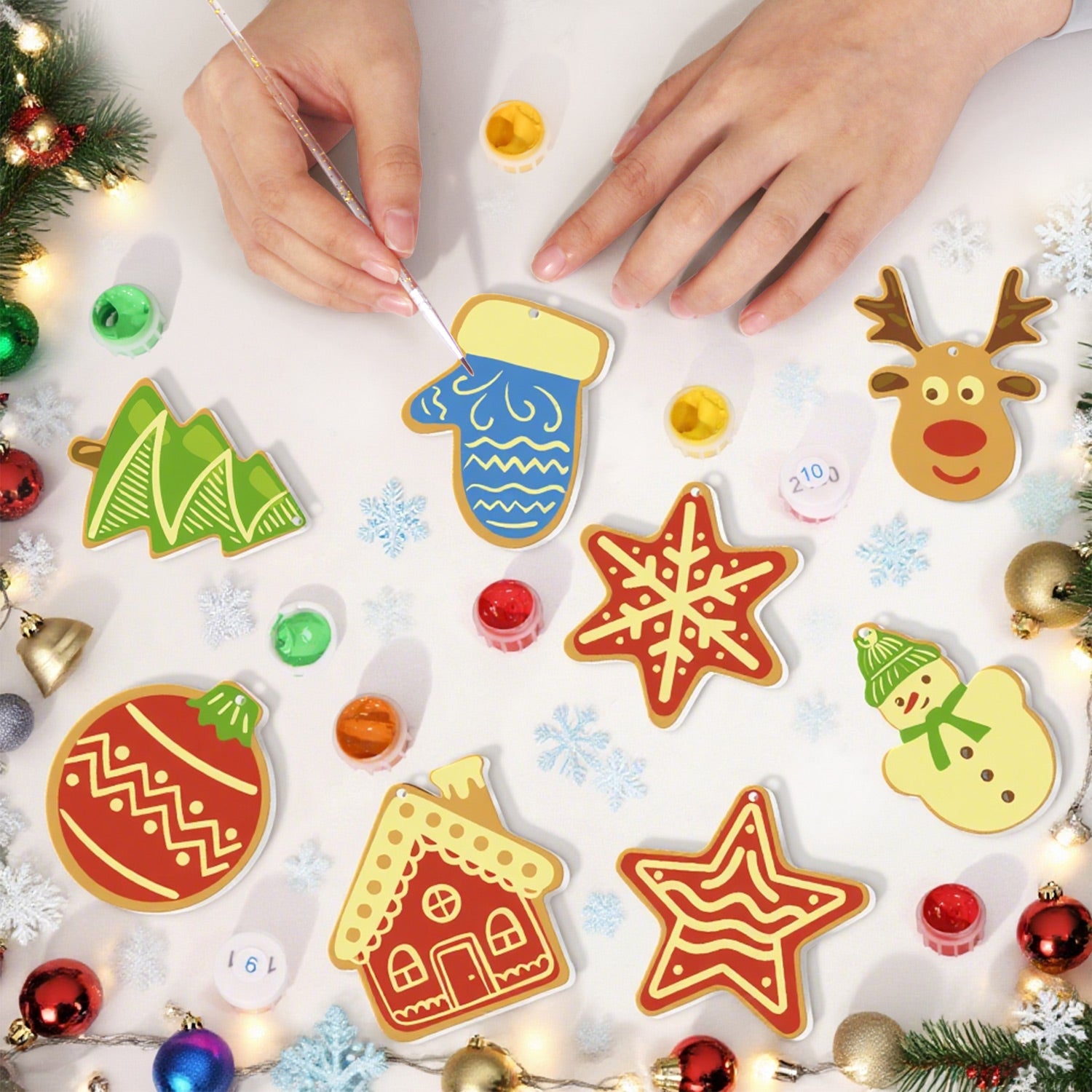 Children's hands painting Christmas-themed ceramic decorations on a white surface with festive decorations around.