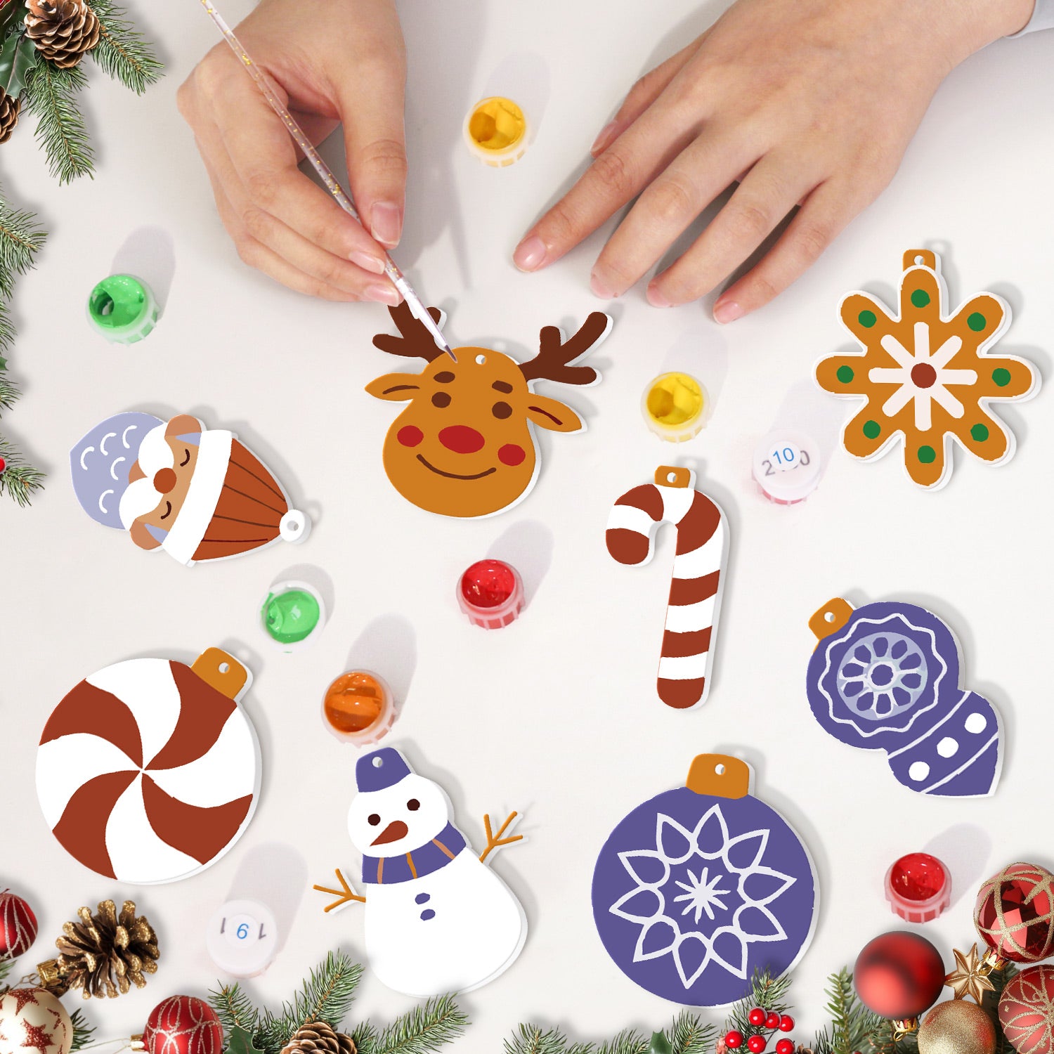 Children's hands decorating Christmas-themed paper ornaments on a white surface with festive decorations around.