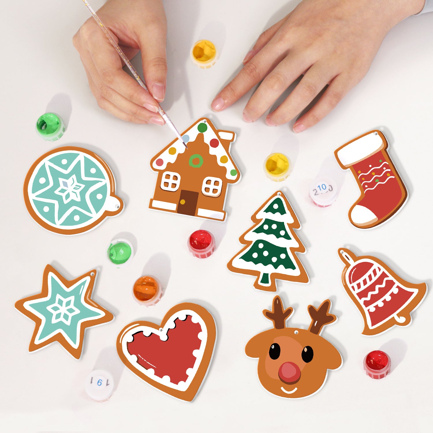 Children's hands painting Christmas-themed paper cutouts on a white surface.