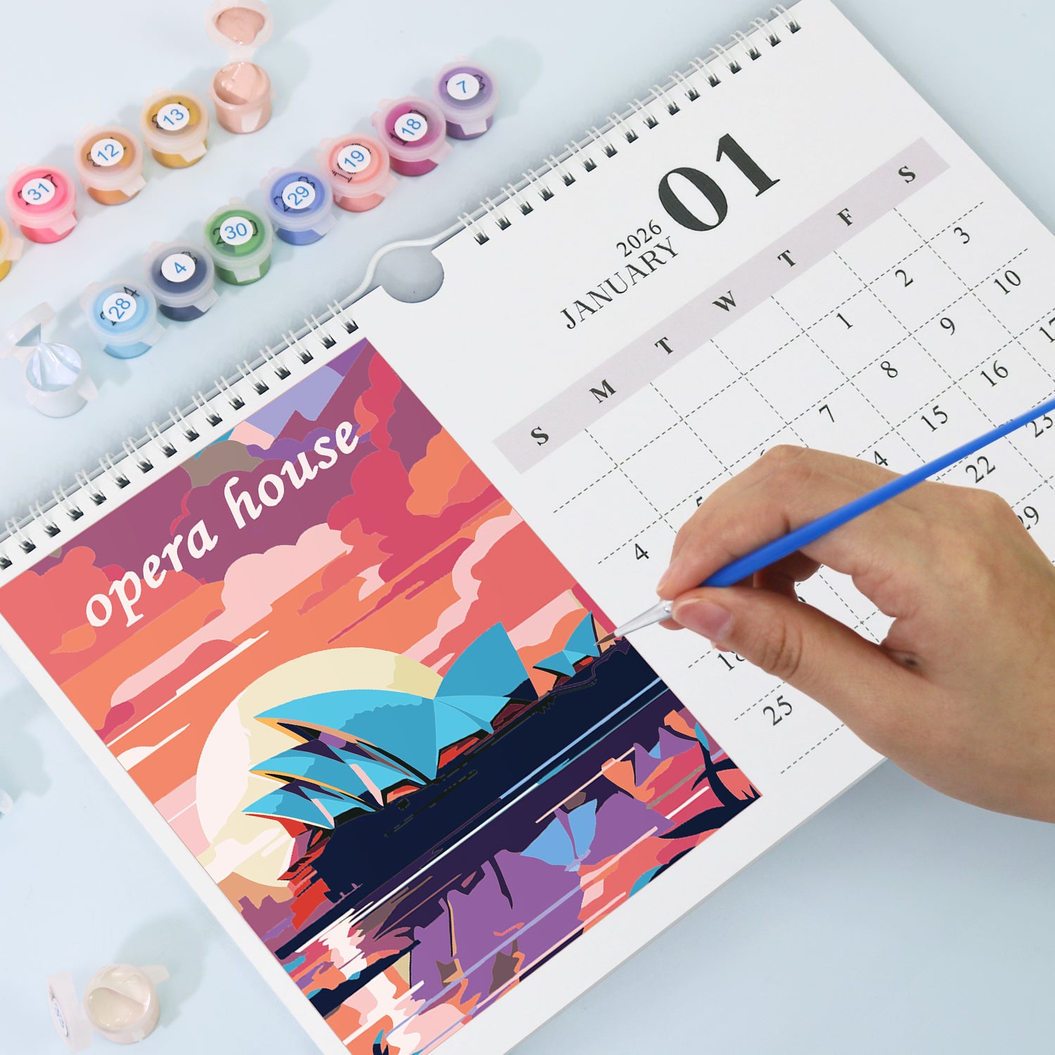 Person coloring a calendar with a Sydney Opera House design, surrounded by art supplies.