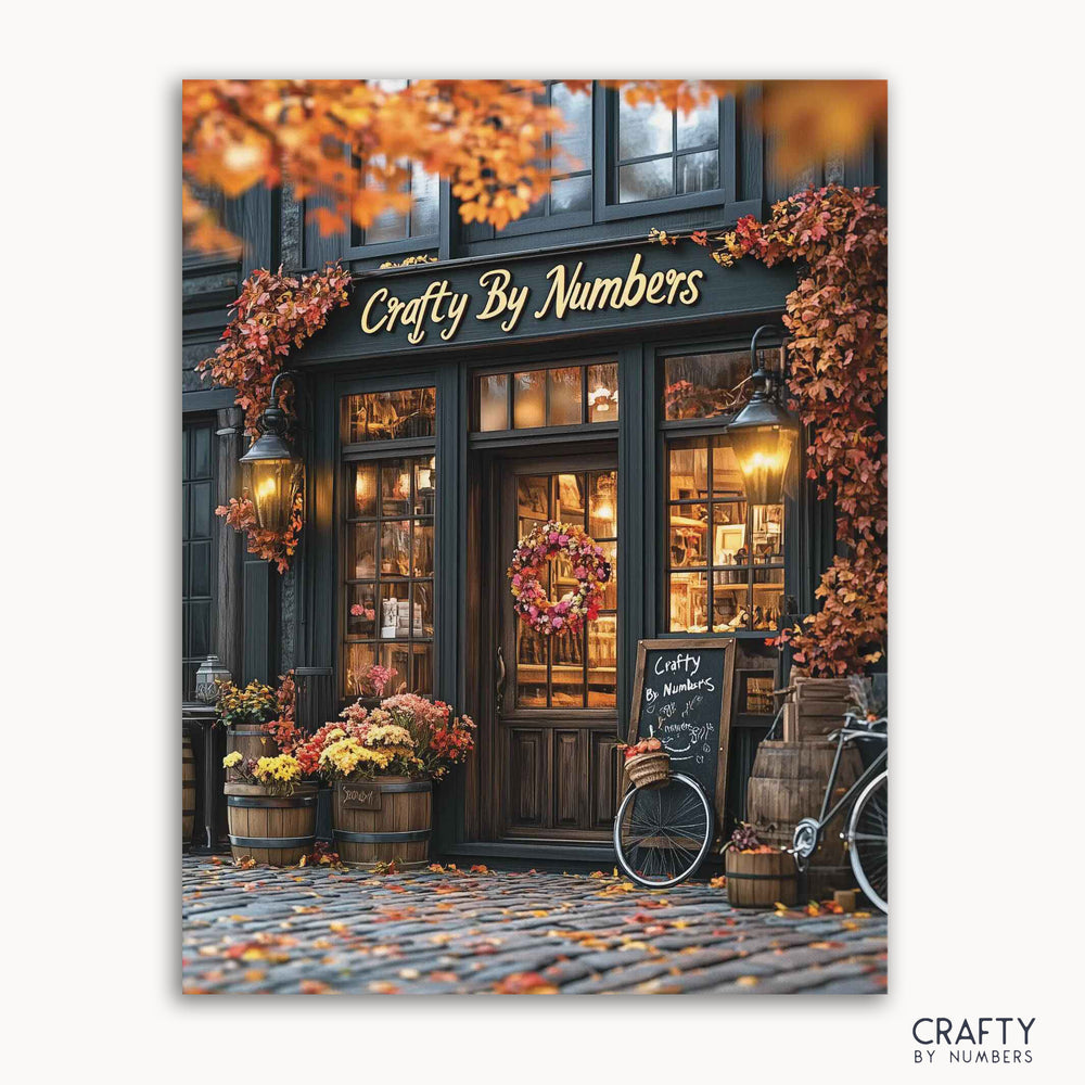 A paint-by-numbers canvas depicting a cozy autumnal storefront scene with fall foliage, pumpkins, and seasonal decor, titled 'Fall Boutique' from Crafty by Numbers.