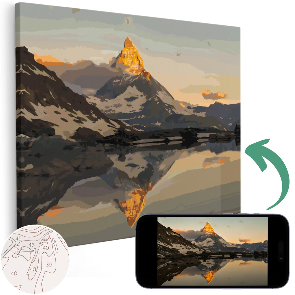 A custom paint by numbers kit depicting a mountain landscape, with a numbered outline on canvas and a mobile phone showing the corresponding landscape photo.