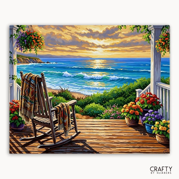 Painting of a coastal scene with a rocking chair, flowers, and a sunset.