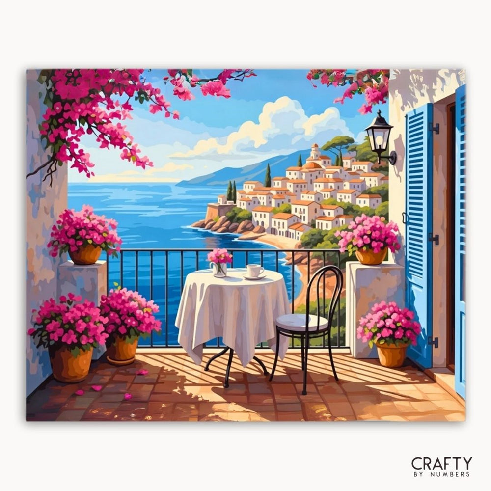 Painting of a coastal scene with a table and chairs on a balcony, surrounded by pink flowers.