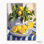 A paint-by-numbers kit image featuring a canvas with a painting of a blue-and-white porcelain pitcher with lemon branches, a glass of lemonade, and a plate with lemons on a striped tablecloth background.