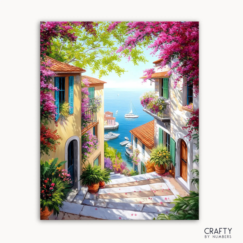 A paint by numbers kit depicting a vibrant scene with colorful flowers, villas, and a view of boats on the water.