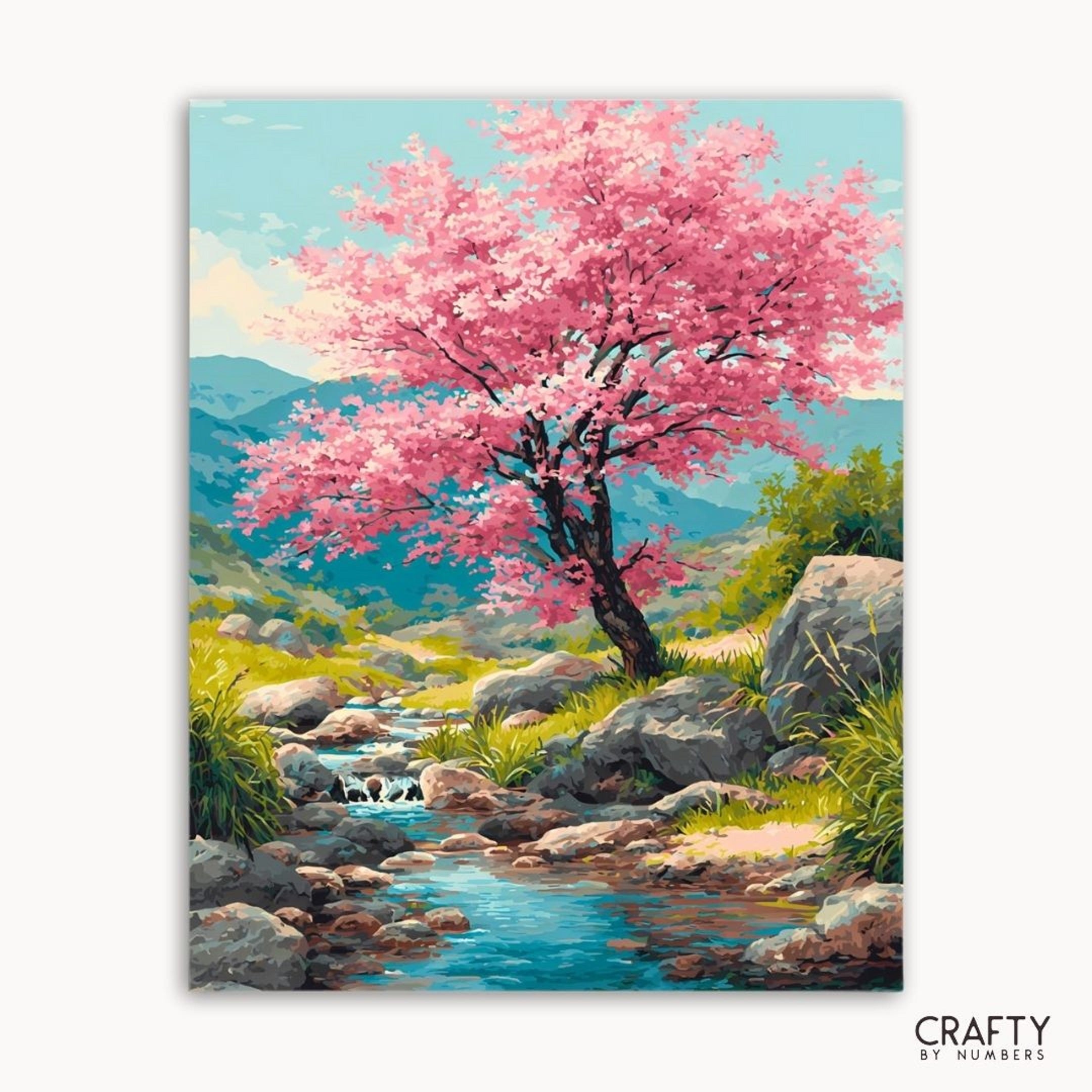 Painting of a cherry blossom tree by a stream with mountains in the background, featuring the brand 'Crafty by Numbers'.