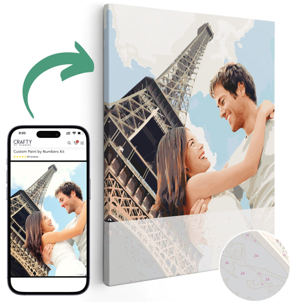 A custom paint by numbers kit depicting a couple embracing in front of the Eiffel Tower, with a smartphone showing the photo being created on the canvas.