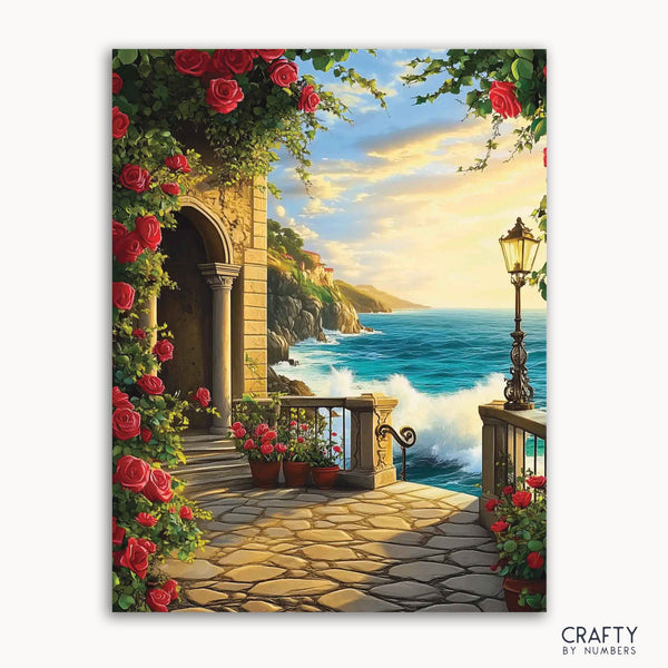 A paint-by-numbers kit depicting a charming seaside terrace with vibrant red roses, stone archways, and ocean waves in the background.