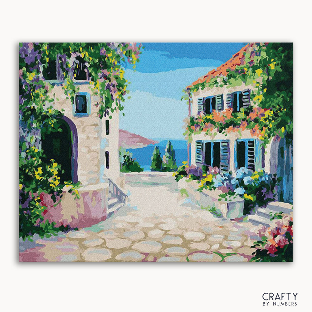 A vibrant painting depicting a picturesque street scene with white buildings, blue shutters, and a clear blue sky, titled 'Santorini Streets' by Crafty by Numbers.
