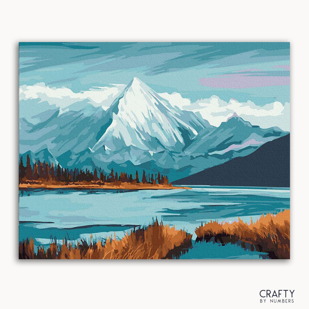 A framed painting depicting a serene mountainous landscape with a lake in the foreground, framed by a mountain range with a blue sky above.