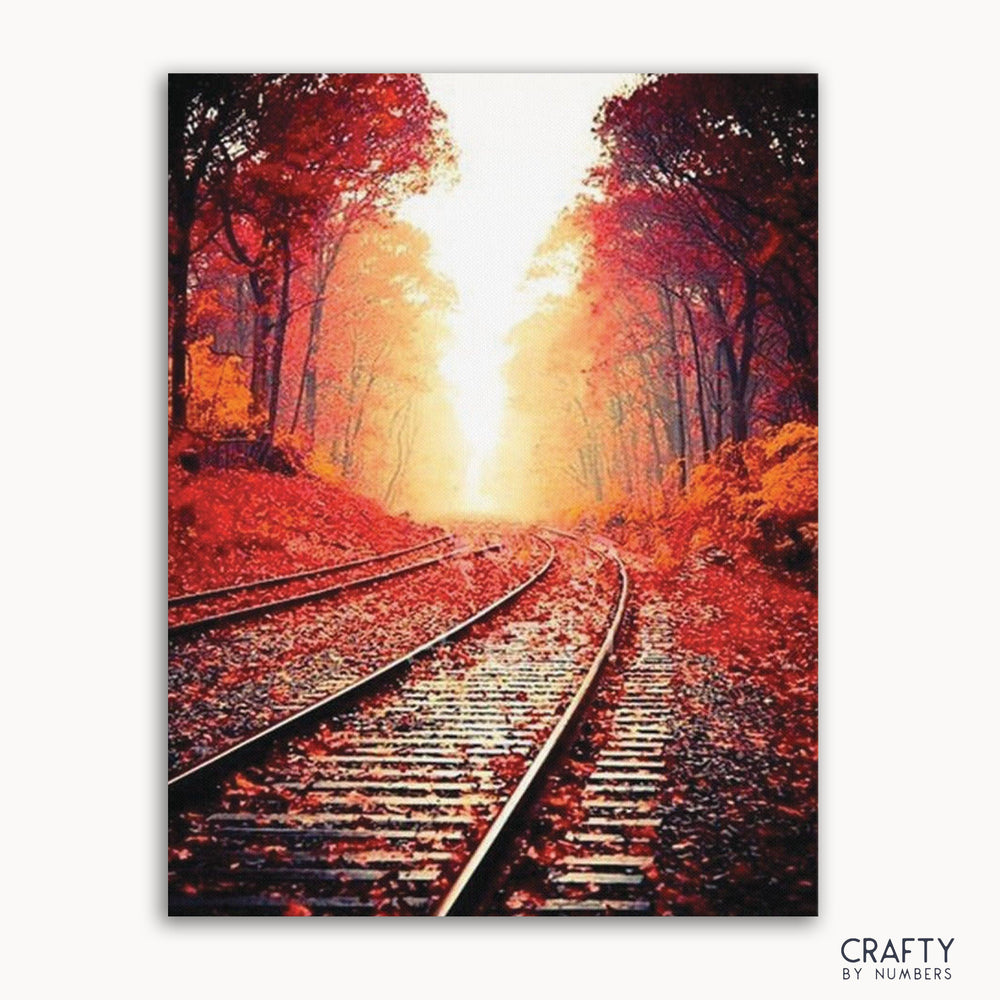 A paint-by-numbers kit image featuring a railway track surrounded by autumn trees with a sunset in the background.
