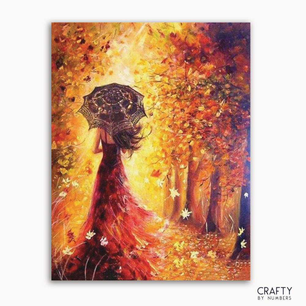A paint by numbers kit depicting a woman with an umbrella walking in a forest during autumn, with vibrant trees and leaves.