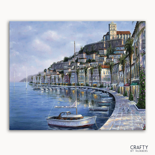 A paint by numbers kit depicting a coastal city scene with buildings, a boat, and the sea.