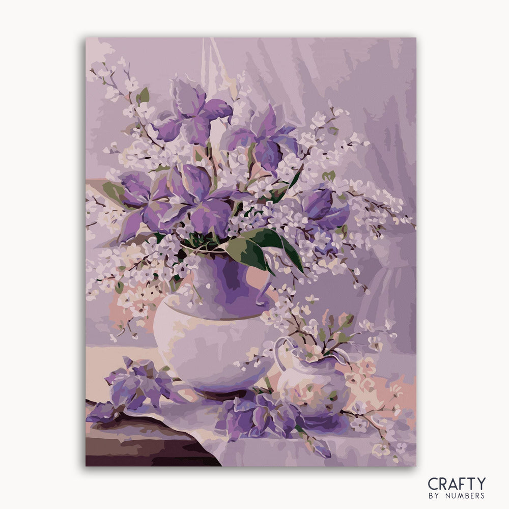 A paint-by-numbers kit image featuring a floral design with purple cornflowers in a vase, with the brand 'CRAFTY by NUMBERS' visible.