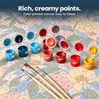 Open acrylic paint pots and three brushes on a canvas with lightly color-printed numbered sections.