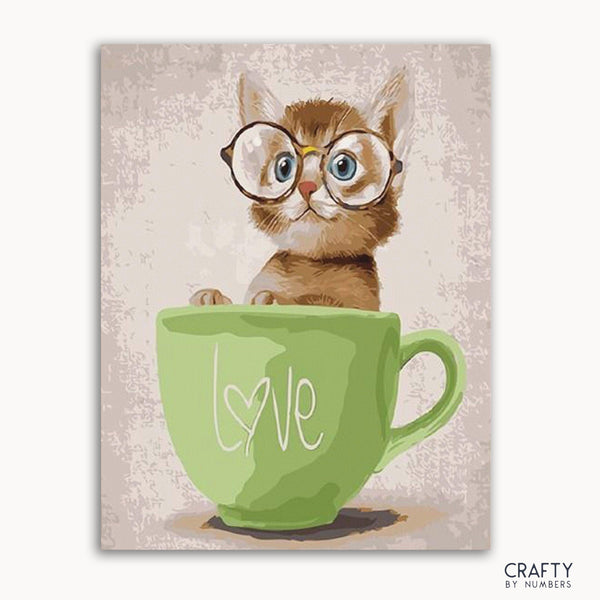 A paint by numbers kit depicting a cute cat with glasses sitting inside a green cup with the word 'love' on it.