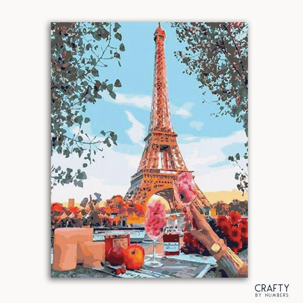 A paint-by-numbers kit image featuring the Eiffel Tower with a colorful foreground, including flowers and a person.