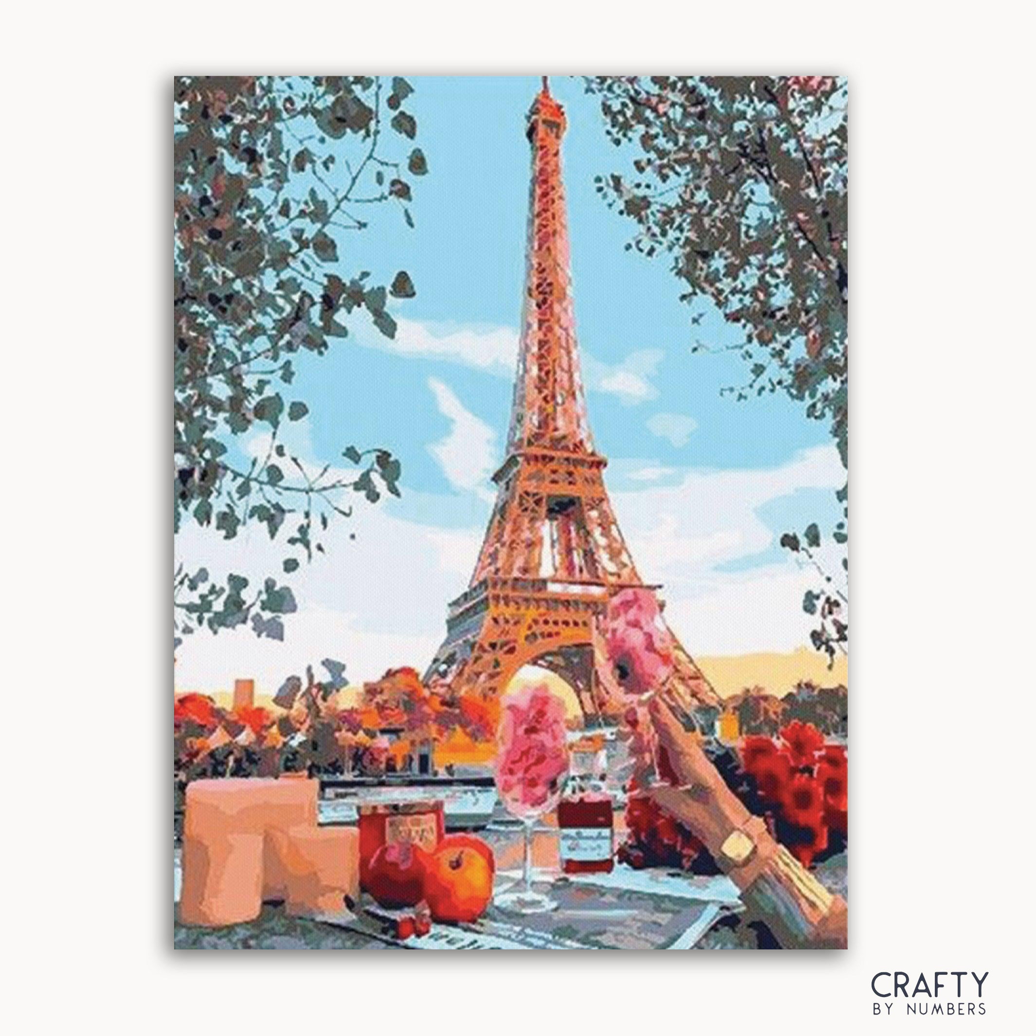 A paint-by-numbers kit image featuring the Eiffel Tower with a colorful foreground, including flowers and a person.
