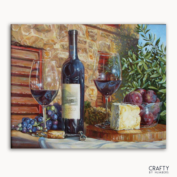 A paint by numbers kit featuring a bottle of wine with glasses filled, assorted fruits, and cheese arranged on a surface with a stone wall background.