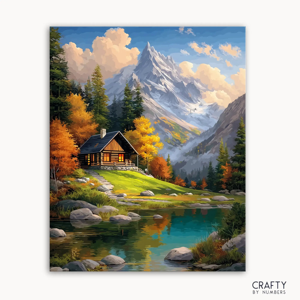 A paint by numbers kit depicting a cabin by a crystal-clear lake with autumn trees and mountains in the background.